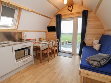 A small kitchen and dining area with a blue couch and glass doors looking out to a grassy field at Bevy in Little Kelk near Bridlington
