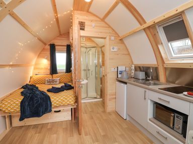 A compact wooden cabin interior with a bed a shower kitchen appliances and a small fridge at Bevy Little Kelk near Bridlington