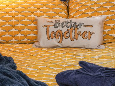 A bed with yellow patterned bedding a cushion with better together text and blue towels