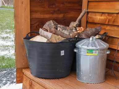 A black plastic container filled with firewood next to a metal trash bin on a wooden porch at Bevy in Little Kelk near Bridlington