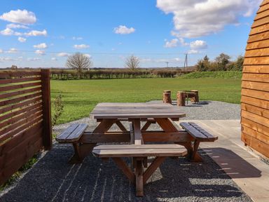 A wooden picnic table on a gravel patio with a grassy field and tree stumps in the background at Bevy in Little Kelk near Bridlington