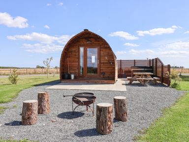 A wooden cabin with a fire pit and log stools in front and a picnic table to the side at Bevy in Little Kelk near Bridlington