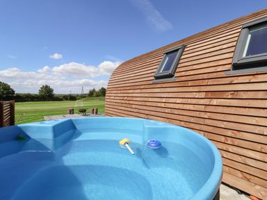 An outdoor hot tub next to a wooden house with a grassy field and soccer goals in the background at Bevy in Little Kelk near Bridlington