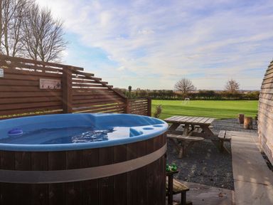 An outdoor area with a hot tub wooden picnic table and a grass field with a soccer goal at Bevy in Little Kelk near Bridlington