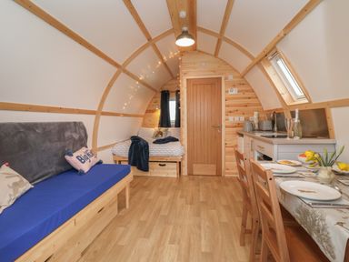 An arched room with a wooden floor a blue sofa a bed a dining table set with plates and a kitchen area Husk Little Kelk near Bridlington