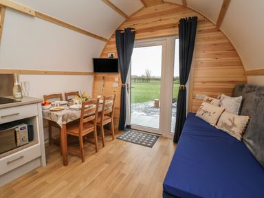A dining table with chairs and tableware beside a blue sofa with cushions in a wooden pod with glass doors and curtains at Husk in Little Kelk near Bridlington