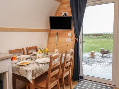A dining area with a wooden table set with plates mugs and flowers next to a door opening to a grassy outdoor area at Husk in Little Kelk near Bridlington
