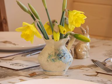 A ceramic pitcher with yellow daffodils on a table with plates cutlery and ceramic rabbit figures at Husk Little Kelk near Bridlington