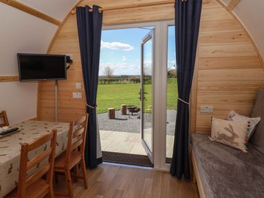 A wooden interior room with a dining table and chairs next to an open glass door with curtains showing a grassy outdoor area at Husk in Little Kelk near Bridlington