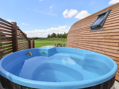An outdoor hot tub with rubber ducks next to a wooden building and a fenced lawn at Husk in Little Kelk near Bridlington