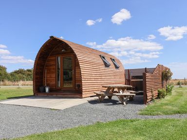 A wooden pod with a picnic table and fenced hot tub outside on a grassy area at Husk Little Kelk near Bridlington