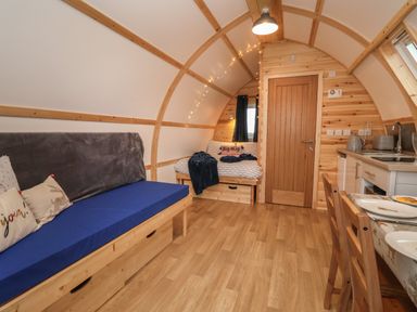 An interior view of a wooden pod with a sofa on the left side a bed in the back a kitchen area on the right and a dining table with chairs at Parliament in Little Kelk near Bridlington