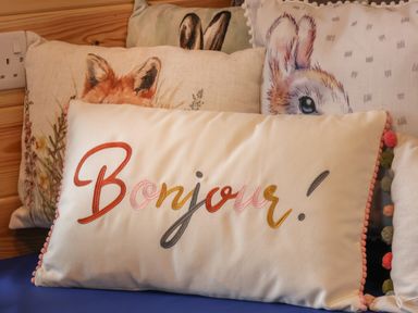 A pillow with the word Bonjour embroidered in multiple colors surrounded by pillows with animal illustrations
