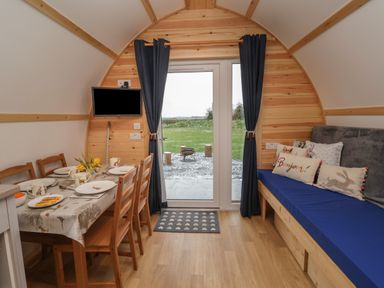 A dining area with a table set for four and a blue cushioned bench with pillows near a glass door with curtains at Parliament in Little Kelk near Bridlington