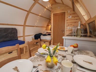 An interior of a small wooden cabin with a dining table set with plates and cups a small kitchenette a door a bed with blankets and pillows and a bench seat at Parliament in Little Kelk near Bridlington