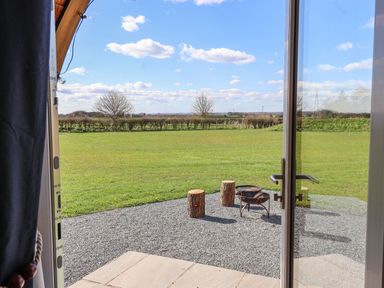 A view of a grassy field with two tree stumps and a fire pit seen through an open glass door at Parliament in Little Kelk near Bridlington