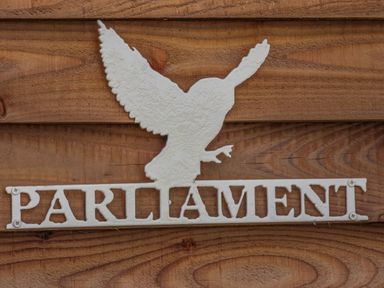 A white metal sign of a bird with wings spread above the word Parliament mounted on wooden boards at Parliament in Little Kelk near Bridlington