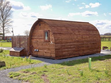 A wooden pod-shaped cabin in a grassy outdoor area with gravel pathways at Parliament in Little Kelk near Bridlington
