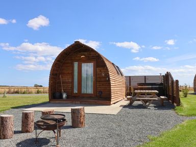 A wooden pod cabin with glass doors surrounded by gravel and grass with a picnic bench and fire pit at Parliament in Little Kelk near Bridlington