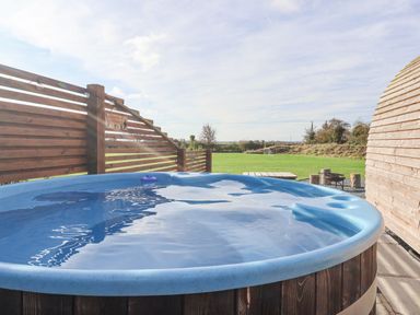 An outdoor hot tub with water inside next to wooden fencing and a green field at Parliament in Little Kelk near Bridlington