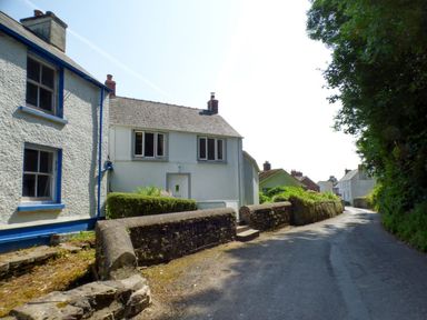 A narrow road lined with stone walls and white houses with blue trim at Spring Garden Cottage in Laugharne