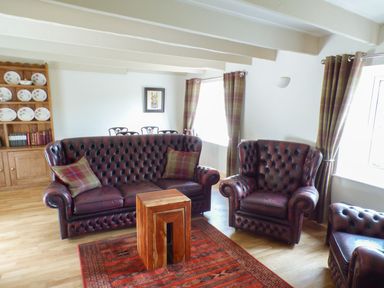 A sitting room with leather sofas wooden table patterned rug and plate rack at Spring Garden Cottage in Laugharne