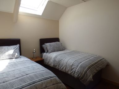 A bedroom with two single beds a wooden nightstand and a skylight window at Spring Garden Cottage in Laugharne