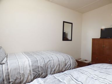 A bedroom with two beds a wall mirror a wooden cabinet with a television and a basket at Spring Garden Cottage in Laugharne
