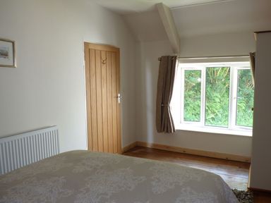 A bedroom with a bed a wooden door a radiator and a window with curtains at Spring Garden Cottage in Laugharne