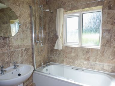 A bathroom with a bathtub shower combination a white sink and a round mirror on marble tiled walls at Spring Garden Cottage in Laugharne