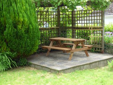 A wooden picnic table on a tiled patio with lattice fencing and green plants at Spring Garden Cottage in Laugharne