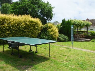 A garden with a ping pong table a rotary clothesline and a wooden bench under a trellis at Spring Garden Cottage in Laugharne