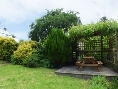 A garden with green bushes and trees and a wooden picnic table under a pergola at Spring Garden Cottage in Laugharne