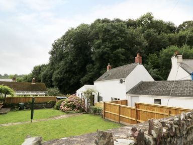 A garden with grass and a stone path next to white houses surrounded by trees at Spring Garden Cottage in Laugharne