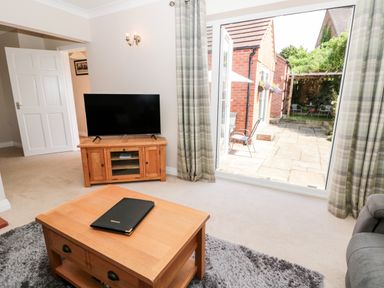 A living room with a wooden coffee table a television on a wooden stand and an open door leading to a patio at Church View in Withernwick near Aldbrough