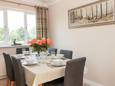 A dining room with a table set for six with flowers and a window with curtains at Church View in Withernwick near Aldbrough