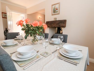A dining table set with white bowls plates cutlery and glasses with a vase of orange roses in a room at Church View Withernwick near Aldbrough