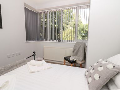 A bedroom with a bed, a chair with a blanket, vertical blinds on windows, and a radiator at Church View in Withernwick near Aldbrough