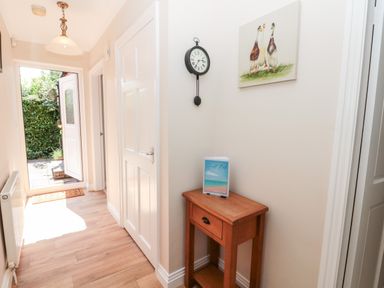 A hallway with a wooden table holding a guest book a wall clock and a painting of ducks at Church View in Withernwick near Aldbrough