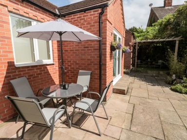 A patio area with a round table umbrella and four chairs outside a red brick house at Church View in Withernwick near Aldbrough