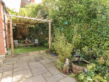 A garden area with a wooden pergola and two chairs around a small table next to a water fountain surrounded by plants at Church View in Withernwick near Aldbrough