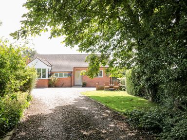 A brick single-story house with a gravel driveway and garden with outdoor chairs at Church View in Withernwick near Aldbrough