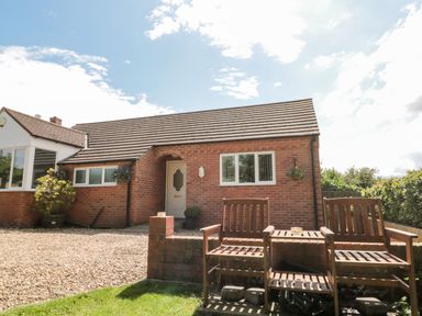 A brick house with a tiled roof and white door two wooden chairs and a small table on a brick patio area at Church View in Withernwick near Aldbrough