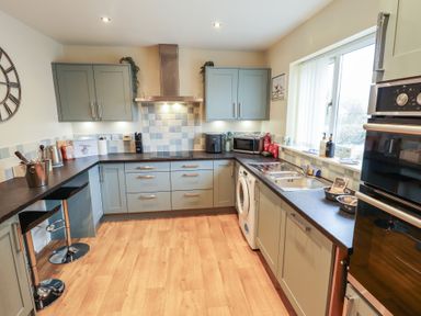 A kitchen with grey cabinets a washing machine a double oven and a window at Church View in Withernwick near Aldbrough