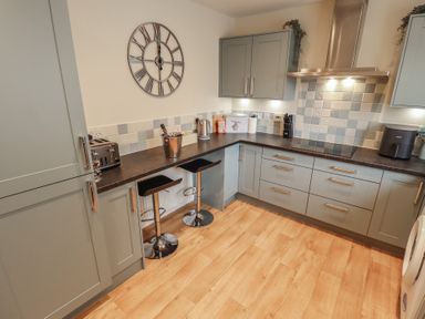 A kitchen with grey cabinets a black countertop two bar stools and a wall clock at Church View in Withernwick near Aldbrough