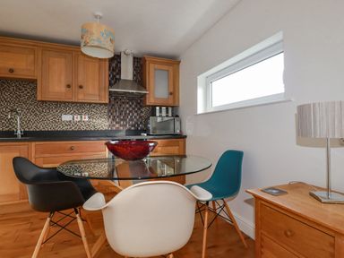 A kitchen with wooden cabinets and a black countertop with a glass table and three chairs at Lapwing in Perranporth