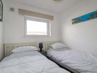A bedroom with two single beds with white bedding and a black lamp on a nightstand between them at Lapwing in Perranporth