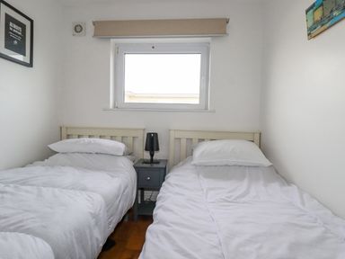 A bedroom with two single beds and a bedside table under a window at Lapwing in Perranporth
