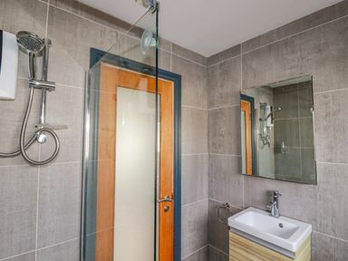 A bathroom with a shower area a wooden door a mirror above a sink and tiled walls at Lapwing in Perranporth