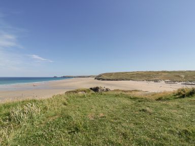 A view of a sandy beach with the ocean on the left and grassy cliffs in the foreground at Lapwing in Perranporth
